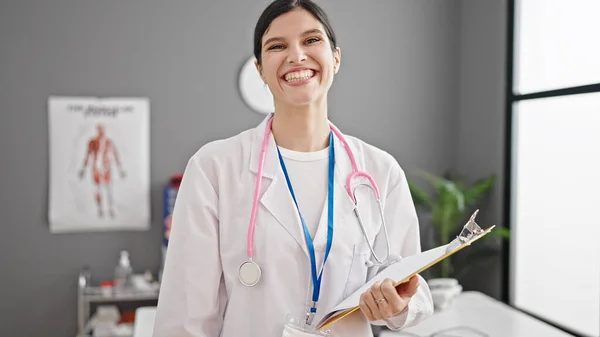 年轻美丽的惊慌失措的女医生微笑着 自信地拿着剪贴板站在诊所 — 图库照片