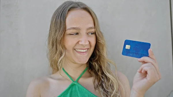Joven Mujer Rubia Sonriendo Confiada Sosteniendo Tarjeta Crédito Sobre Fondo —  Fotos de Stock