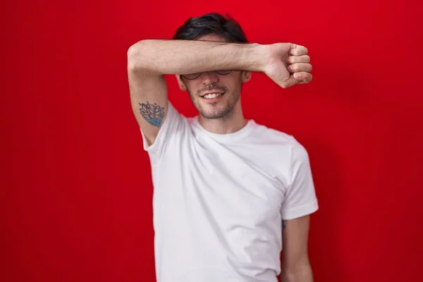 若いヒスパニック系の男は腕が陽気で面白い笑顔で目をカバー赤い背景の上に立っている 視覚障害の概念 — ストック写真