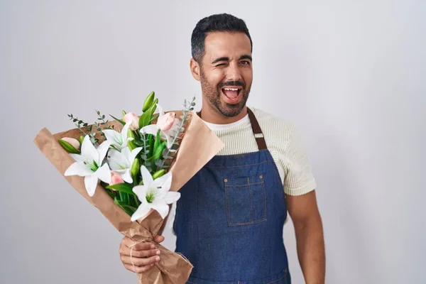 Hispanic man with beard working as florist winking looking at the camera with sexy expression, cheerful and happy face.