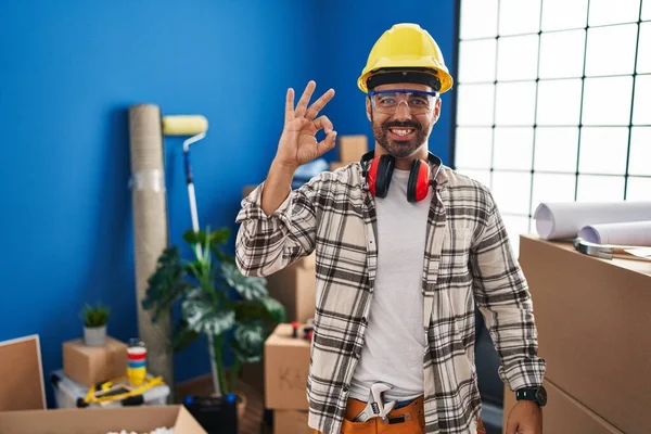 髭を生やした若いヒスパニック系の男が手と指でOkサインをして笑顔で自宅の改装で働いています 成功した表現 — ストック写真