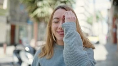 Young blonde woman smiling confident combing hair with hands at street