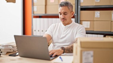 Ofiste dizüstü bilgisayar kullanan Latin asıllı genç bir iş adamı.