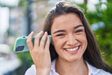 Young hispanic woman smiling confident listening audio message by the smartphone at park