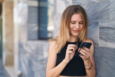 Sokakta gülümseyen akıllı telefon kullanan genç sarışın kadın.
