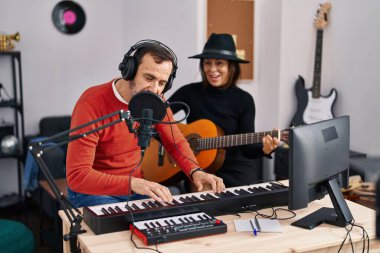 Middle age man and woman musicians playing guitar and keyboard piano singing song at music studio