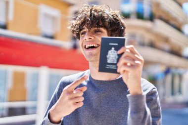 Genç İspanyol adam gülümsüyor. Sokakta kendini göstererek Kanada pasaportunu işaret ediyor.
