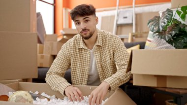 Genç Arap adam yeni evinde karton kutuları açıyor.