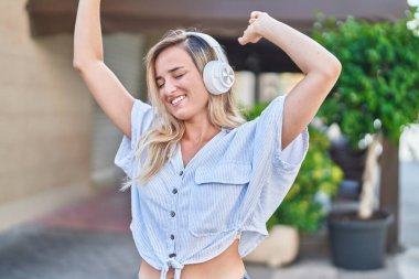 Young blonde woman listening to music and dancing at street