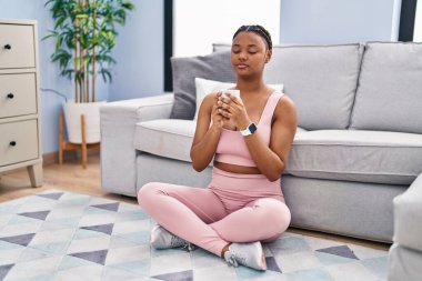 African american woman drinking coffee sitting on floor at home