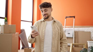 Genç Arap adam yeni evinde akıllı telefon kullanarak kendinden emin gülümsüyor.