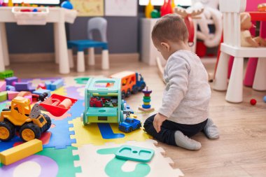 Anaokulunda yerde oturan sevimli İspanyol çocuk araba oyuncağıyla oynuyor.