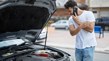 Genç İspanyol adam akıllı telefondan konuşuyor. Sokakta araba arızası sigortası var.