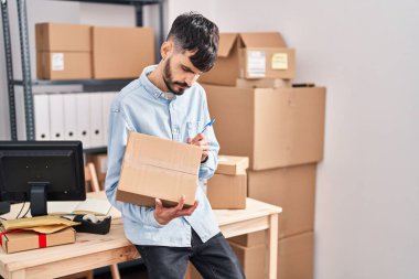 Latin kökenli genç bir iş adamı iş yerinde paket üzerine yazıyor.