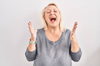 Orta yaşlı beyaz bir kadın beyaz arka planda deli deli deli bağırıyor ve agresif bir ifade ve kollarla bağırıyor. hüsran kavramı. 