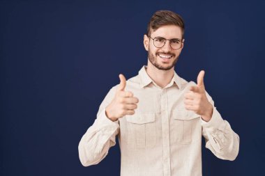 Mavi arka planda sakallı İspanyol bir adam mutlu ve komik yüzüyle kamerayı işaret ediyor. iyi enerji ve titreşimler. 