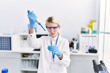 Laboratuvarda test tüpüne sıvı döken genç sarışın bilim kadını.