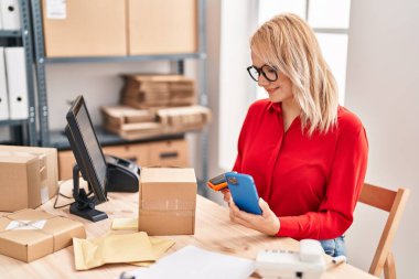 Genç sarışın kadın ecommerce iş çalışanı ofiste akıllı telefon kullanarak paket tarama