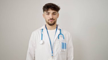 İzole edilmiş beyaz arka plan üzerinde gevşek bir ifadeyle duran genç Arap doktor.