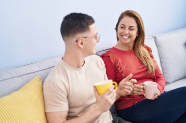 Man and woman mother and son drinking coffee sitting on sofa at home