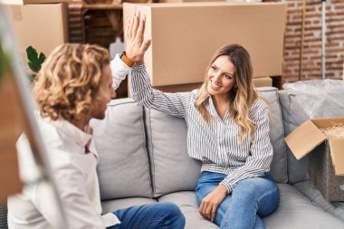 Man and woman couple high five with hands raised up sitting on sofa at new home