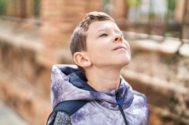 Sarışın çocuk, kendinden emin bir şekilde caddede gökyüzüne bakıyor.