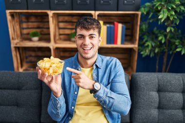 Elinde patates cipsi tutan genç İspanyol adam mutlu bir şekilde elini ve parmağını gösterdi. 