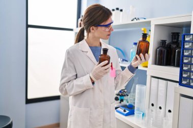 Genç sarışın bilim adamı laboratuvarda sıvı şişeler tutuyor.