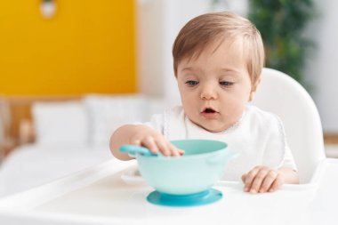 Sevimli beyaz bebek yatak odasında elinde kaşıkla sandalyede oturuyor.
