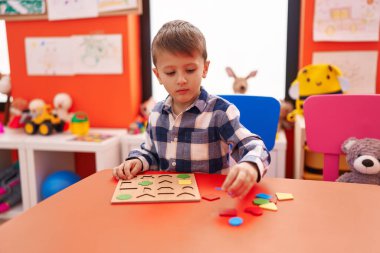Anaokulunda masada oturmuş matematik oyunu oynayan sevimli beyaz çocuk.