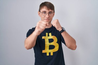 Kafkasyalı sarışın adam bitcoin tişört giyiyor dövüşmek için yumruk atıyor agresif ve öfkeli saldırı, tehdit ve şiddet 