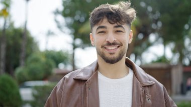 Genç Arap adam parkta kendine güvenerek gülümsüyor.