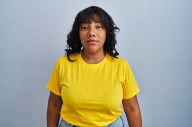 Hispanic woman standing over blue background relaxed with serious expression on face. simple and natural looking at the camera. 
