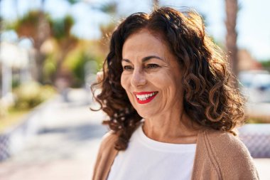 Orta yaşlı İspanyol kadın dışarıda mutlu bir şekilde gülümsüyor.