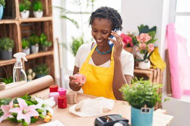 Middle age african american woman florist talking on smartphone holding gift lace at flower shop