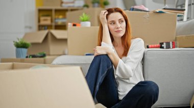 Yeni evinde ciddi bir ifadeyle kanepede oturan genç kızıl saçlı kadın.