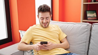 Evdeki kanepede oturan, akıllı telefon kullanan genç bir İspanyol.