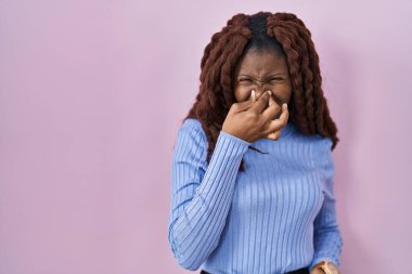 Pembe arka planda dikilen Afrikalı kadın pis ve iğrenç bir koku alıyor. Nefesini burnunda tutuyor. Kötü kokuyor. 