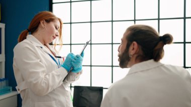 Bilim adamı üniforması giyen kadın ve erkek laboratuarda panoya yazı yazıyorlar.