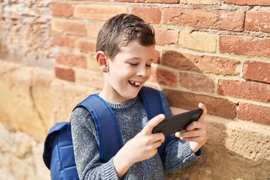 Sarışın çocuk sokakta akıllı telefon kullanıyor.
