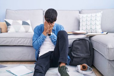 Genç İspanyol bir adam yerde oturmuş, üniversite için çalışıyor. Suratı ağlarken elleriyle yüzünü kapatıyor. depresyon kavramı. 