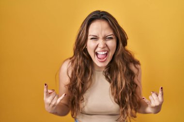 Sarı arka planda dikilmiş deli gibi bağıran genç İspanyol kadın elleri havada rock sembolü yapıyor. Müzik yıldızı. ağır kavram. 