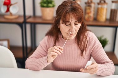Middle age woman doing antigen covid-19 test sitting on table at home