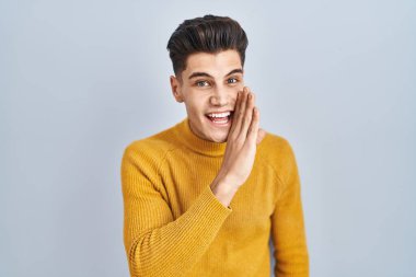 Latin asıllı genç bir adam mavi arka planda el ele tutuşup gizli söylentiler yayıyor, kötü niyetli konuşmalar fısıldıyor. 