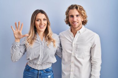 Mavi arka planda duran genç çift, mutlu ve kendinden emin gülümserken beş numarayı gösterip işaret ediyor.. 