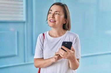 Sokakta akıllı telefon kullanan orta yaşlı bir kadın gülümsüyor.