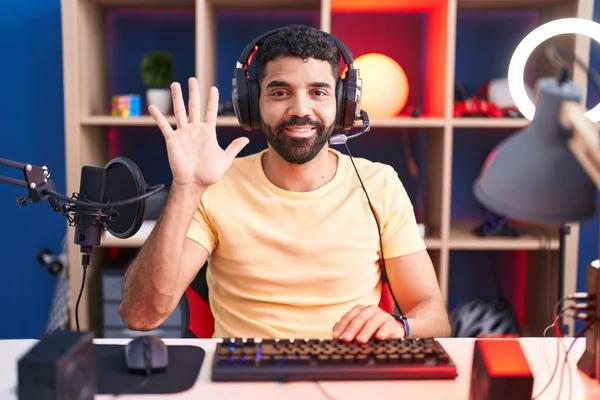 自信と幸せ笑みを浮かべている間 ヘッドフォンでビデオゲームをプレイし 指の数5を指しているヒスパニック男 — ストック写真