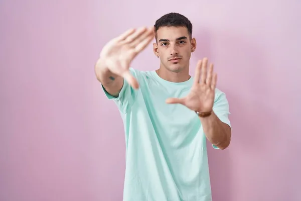 stock image Handsome hispanic man standing over pink background doing frame using hands palms and fingers, camera perspective 