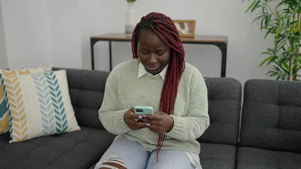 Αφρικανική Γυναίκα Πλεγμένα Μαλλιά Χρησιμοποιώντας Smartphone Κάθεται Στον Καναπέ Στο — Φωτογραφία Αρχείου