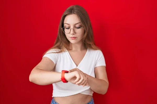年轻的高加索女人站在红色的背景下 用腕表检查时间 放松而自信 — 图库照片